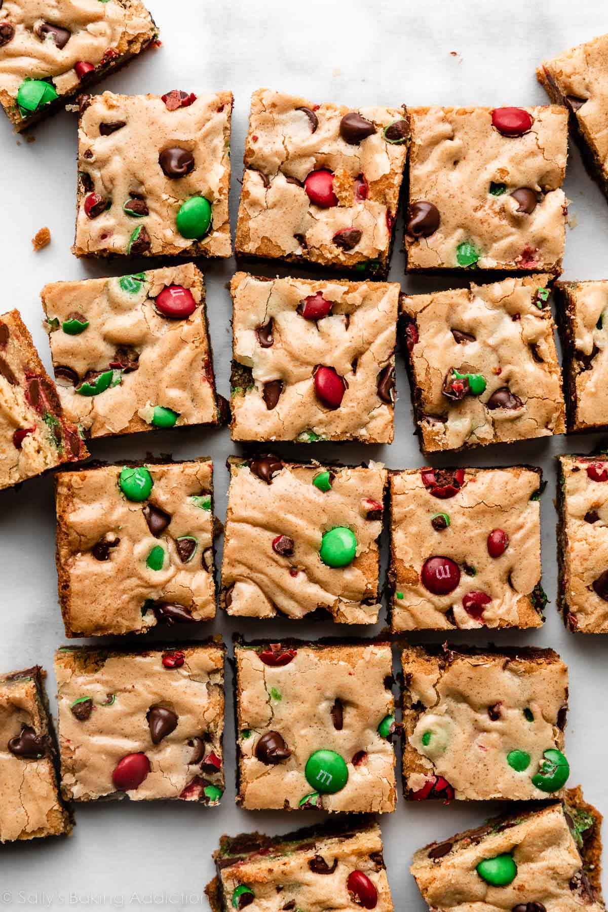 sliced M&M cookie bar squares on parchment with chocolate chips and Christmas M&Ms.