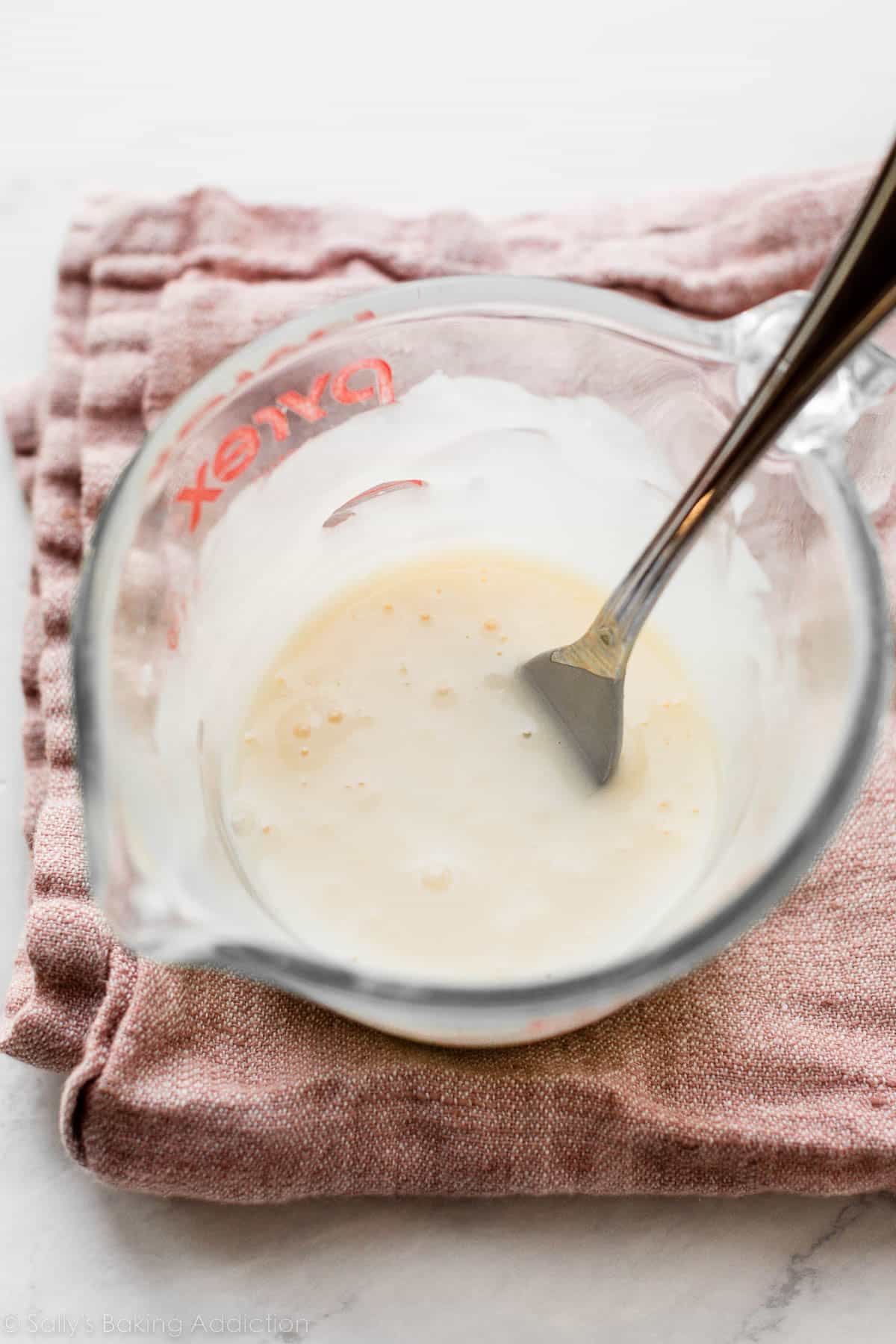 icing and fork in liquid measuring up on pink linen.