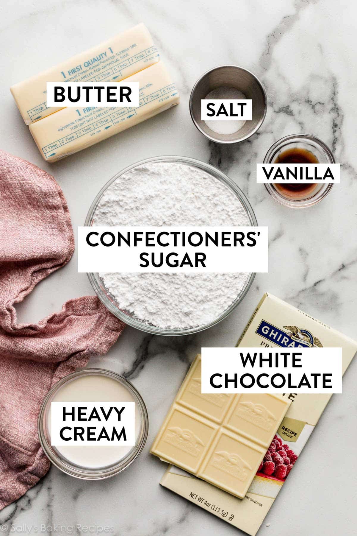 ingredients on marble counter including white chocolate, confectioners' sugar, butter, salt, vanilla, and heavy cream.