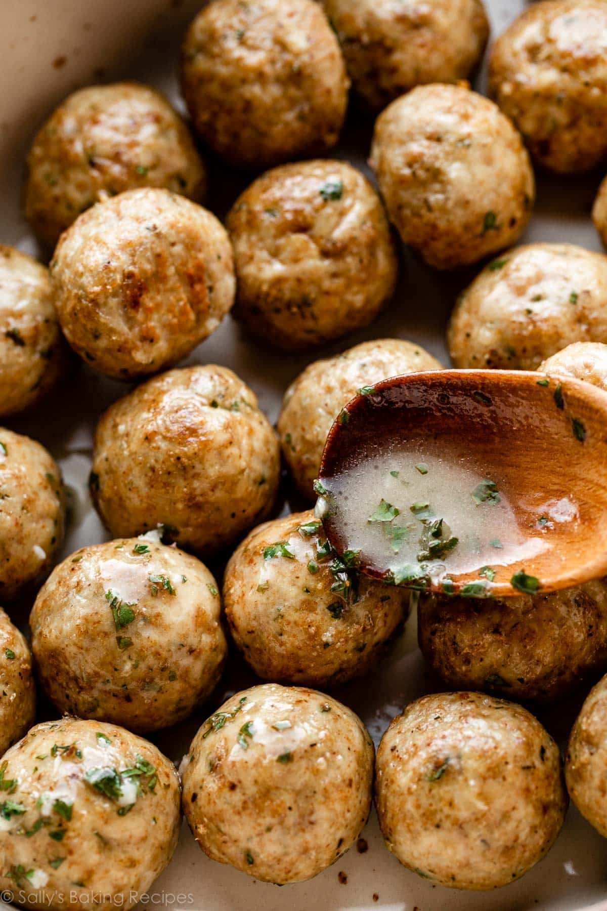 meatballs on platter with spoon drizzling herb butter sauce on top of one.