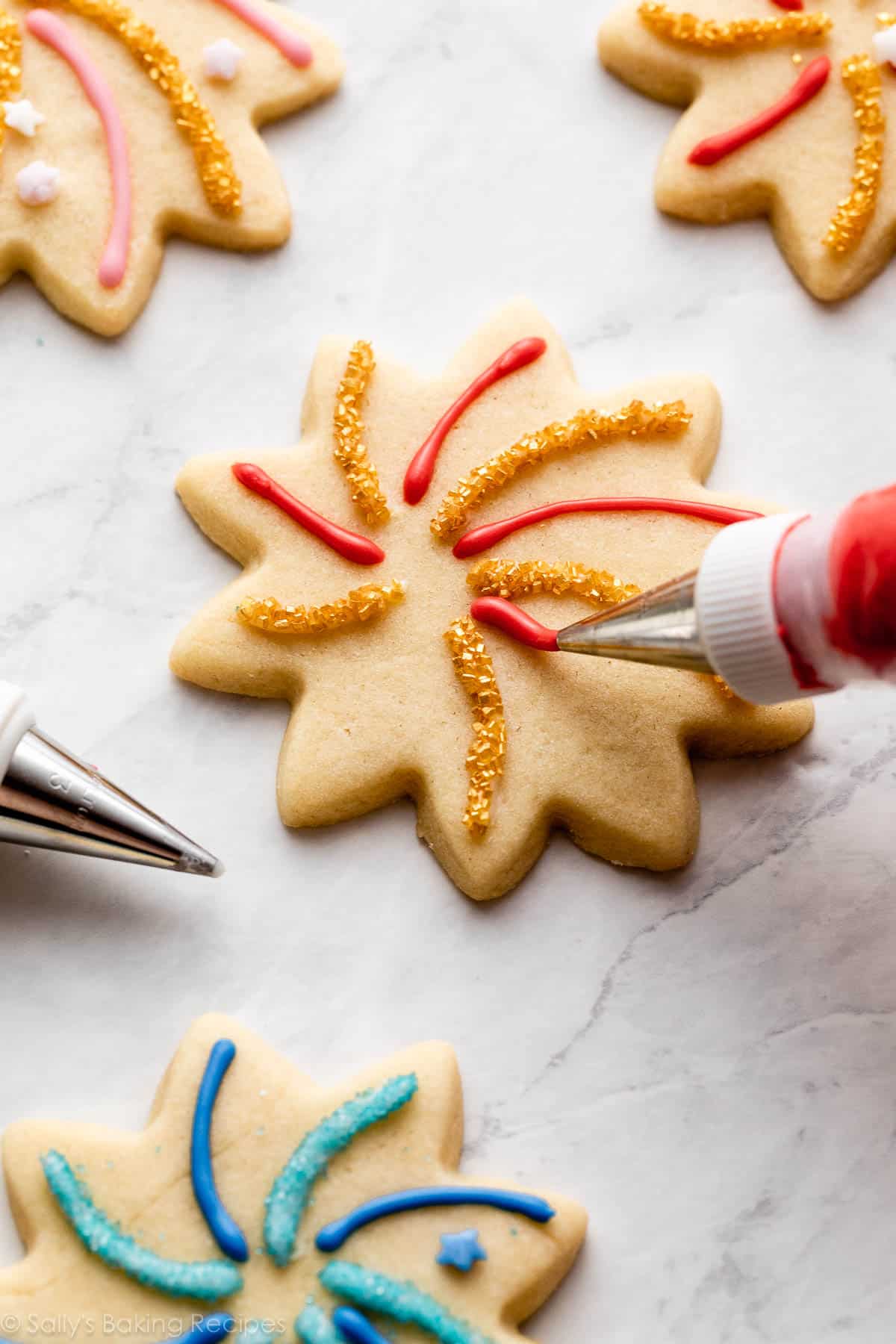 piping tip piping red icing on flower-shaped cookie.