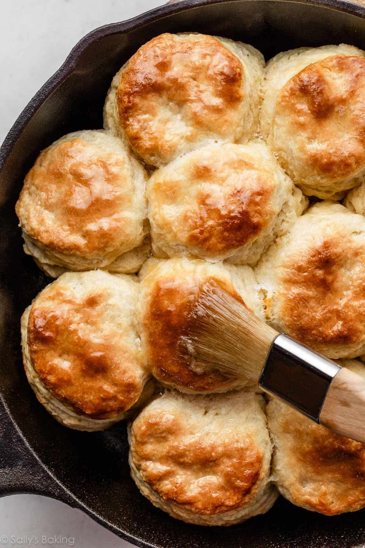 homemade biscuits in cast iron skillet being brushed with melted butter.
