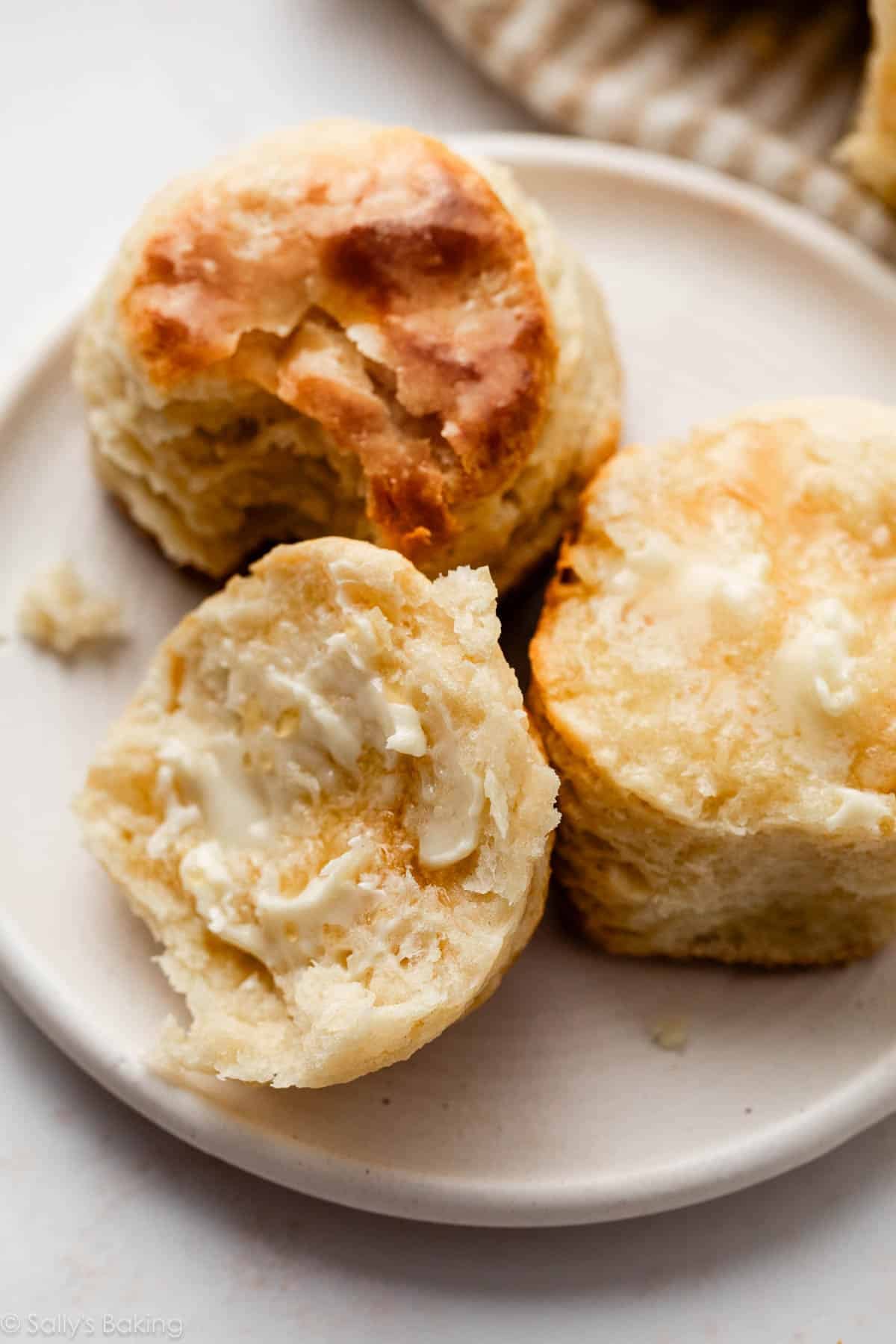 homemade biscuit cut in half with butter on it on white plate.