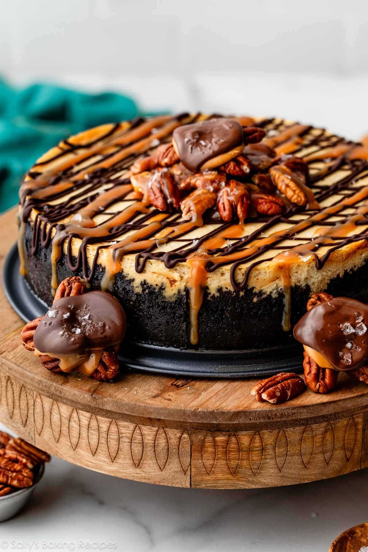 side view of caramel pecan turtle cheesecake with chocolate turtle candies around it.