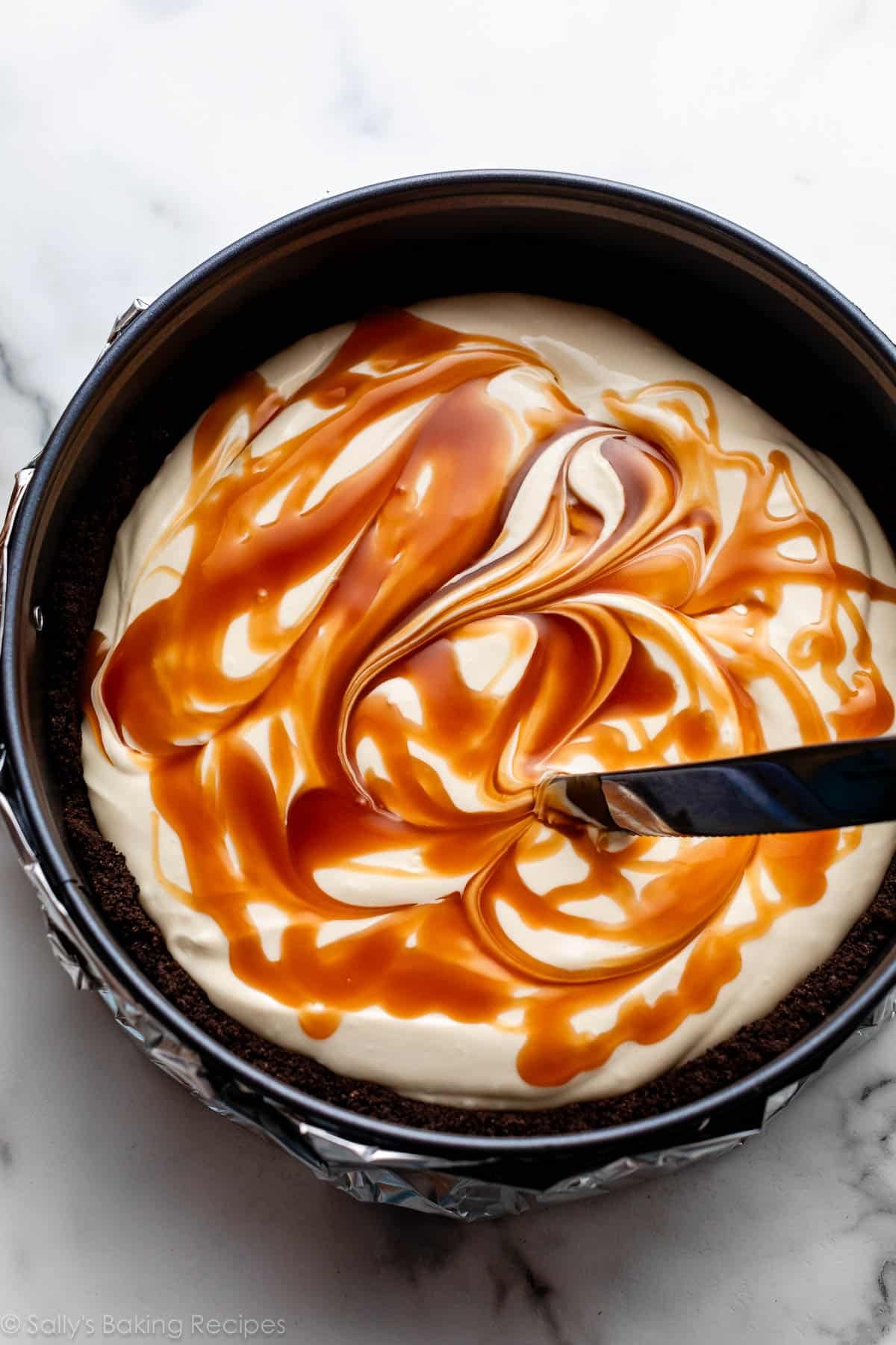 knife swirling caramel into cheesecake batter in Oreo crust.