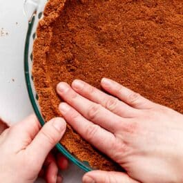 hands pressing Biscoff cookie pie crust into glass pie dish.
