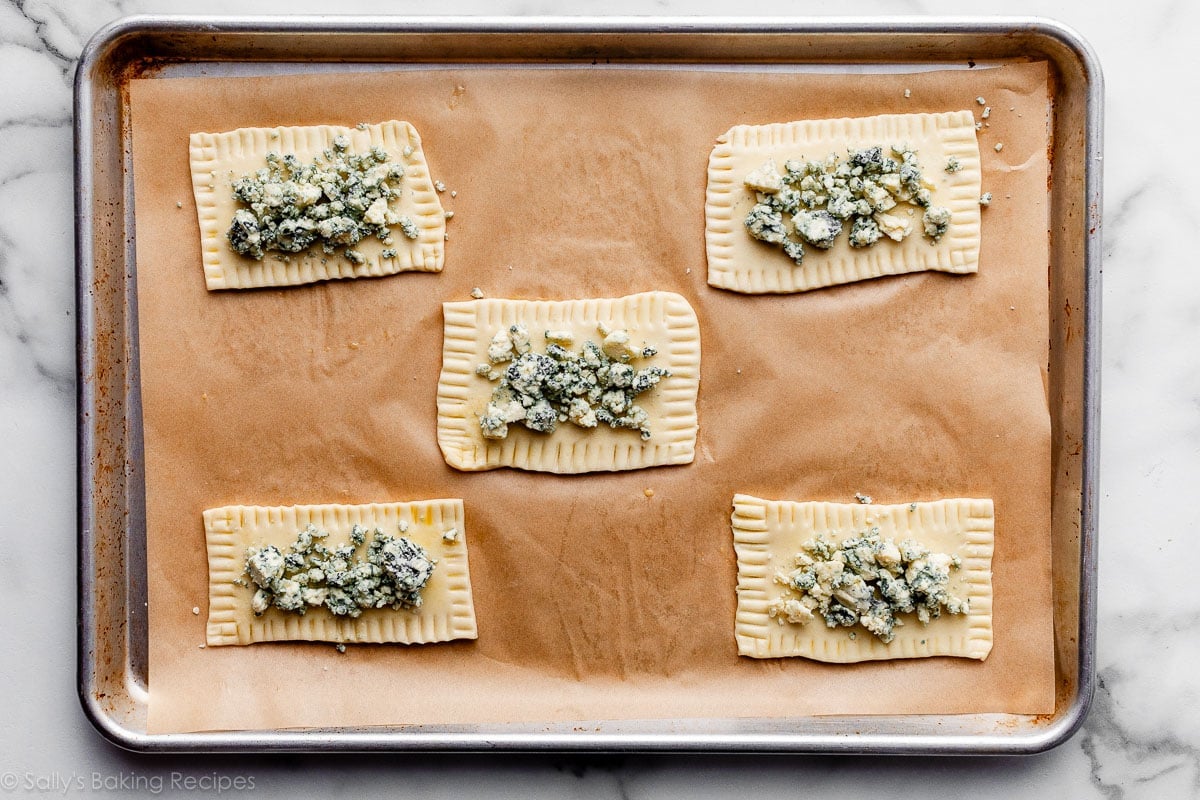 crumbled gorgonzola cheese on top of 5 dough rectangles on lined baking sheet.