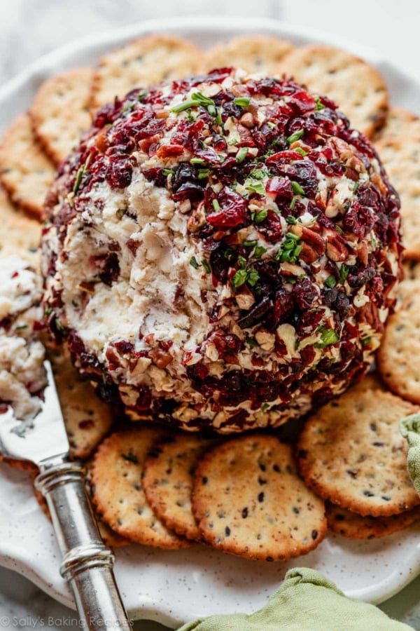 cranberry white cheddar cheese ball cut open with crackers on plate.