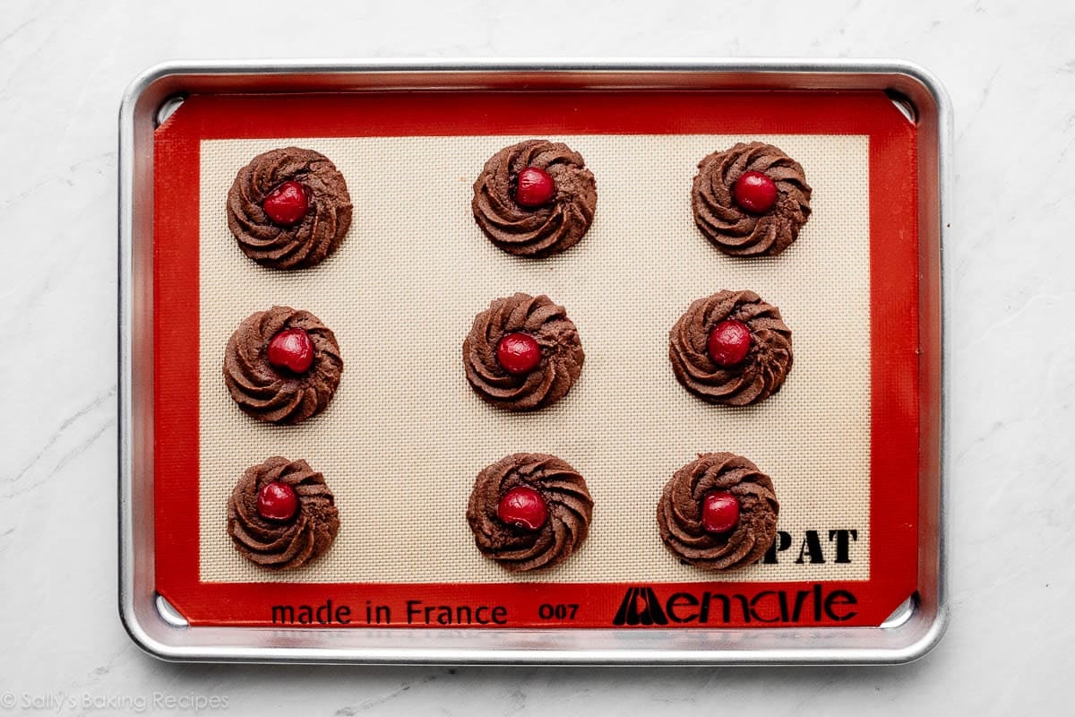 piped chocolate cookies on lined baking sheet.