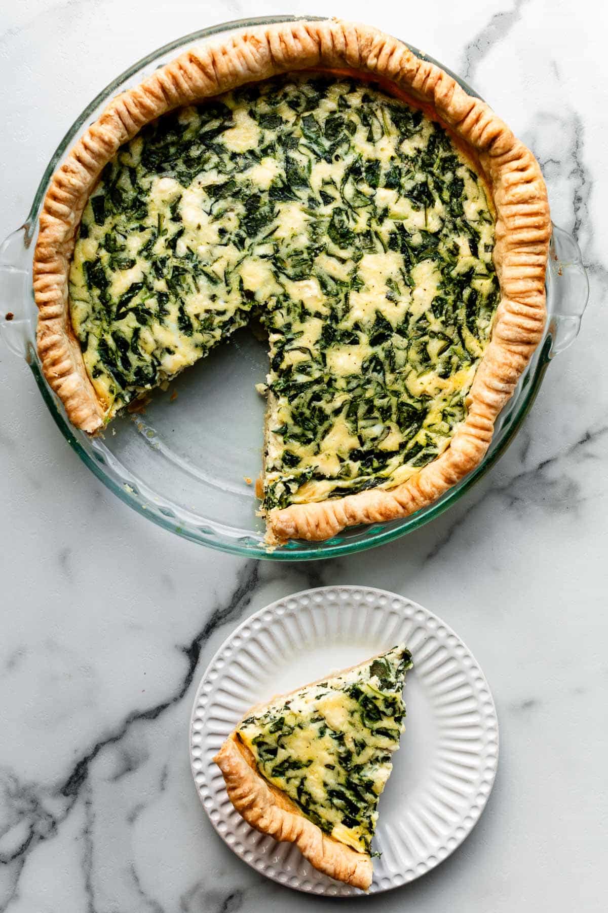 spinach quiche with slice cut out and set on plate.