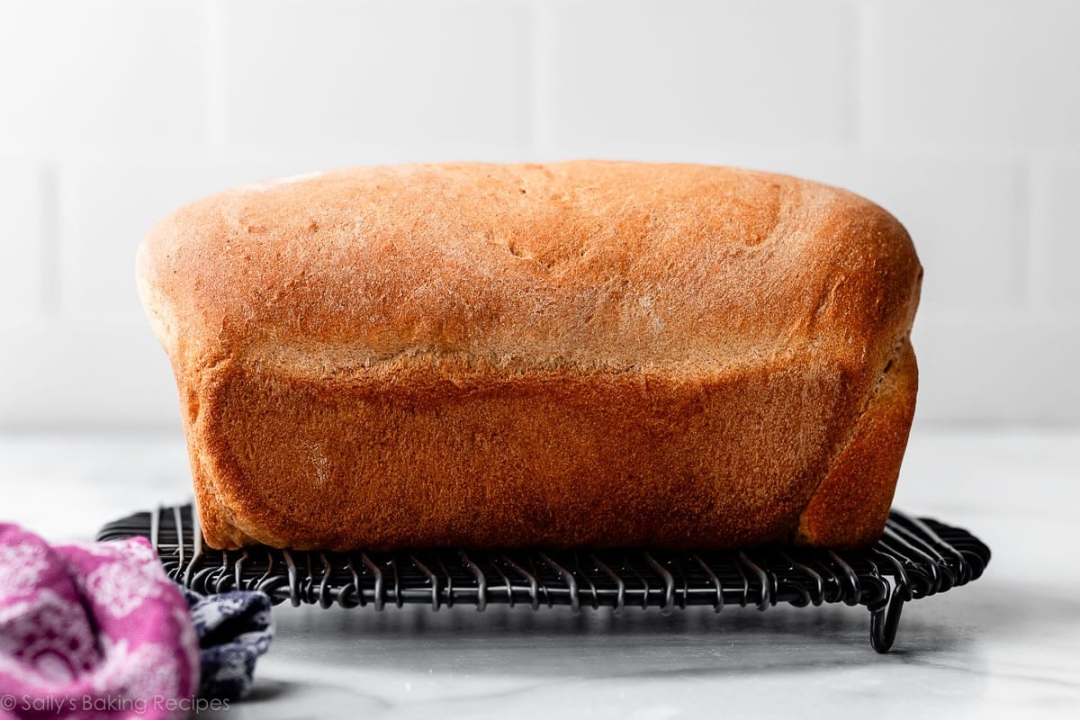 loaf of bread on black wire cooling rack with purple linen in foreground.