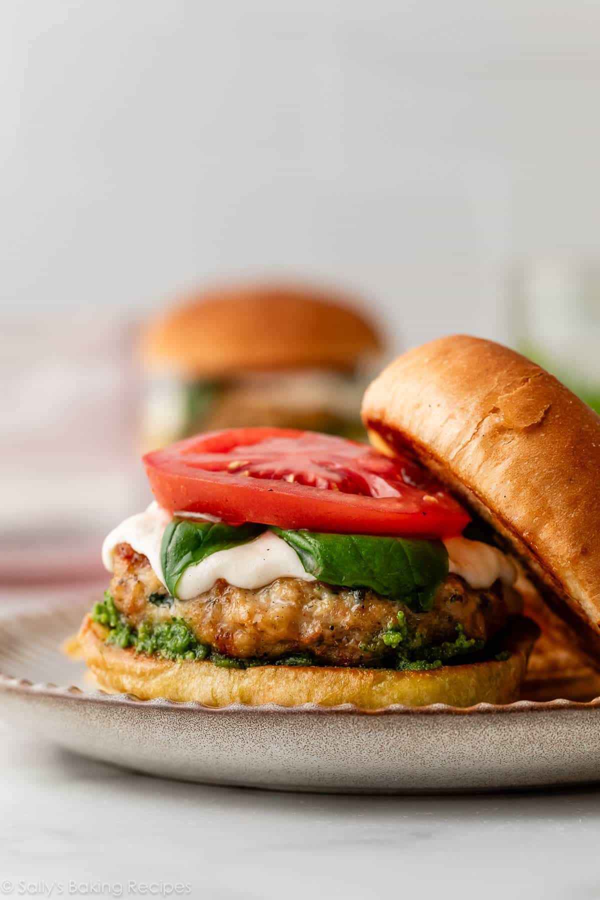 caprese pesto chicken burger open face on bun with mozzarella cheese, basil, and tomato on top.