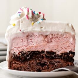 slice of ice cream cake with whipped cream and sprinkles on top on white plate.