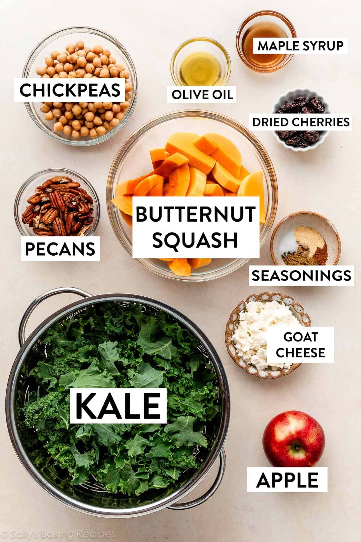 ingredients on beige surface including butternut squash, apple, dried cherries, pecans, goat cheese, and chickpeas.
