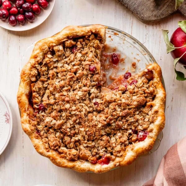 apple cranberry crumble pie with slice taken out on wooden surface.