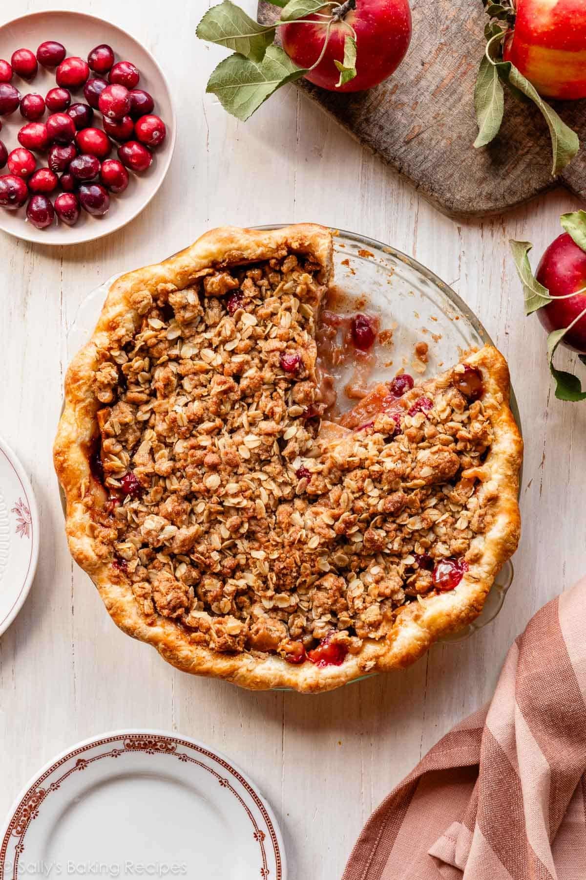 apple cranberry crumble pie with slice taken out on wooden surface.