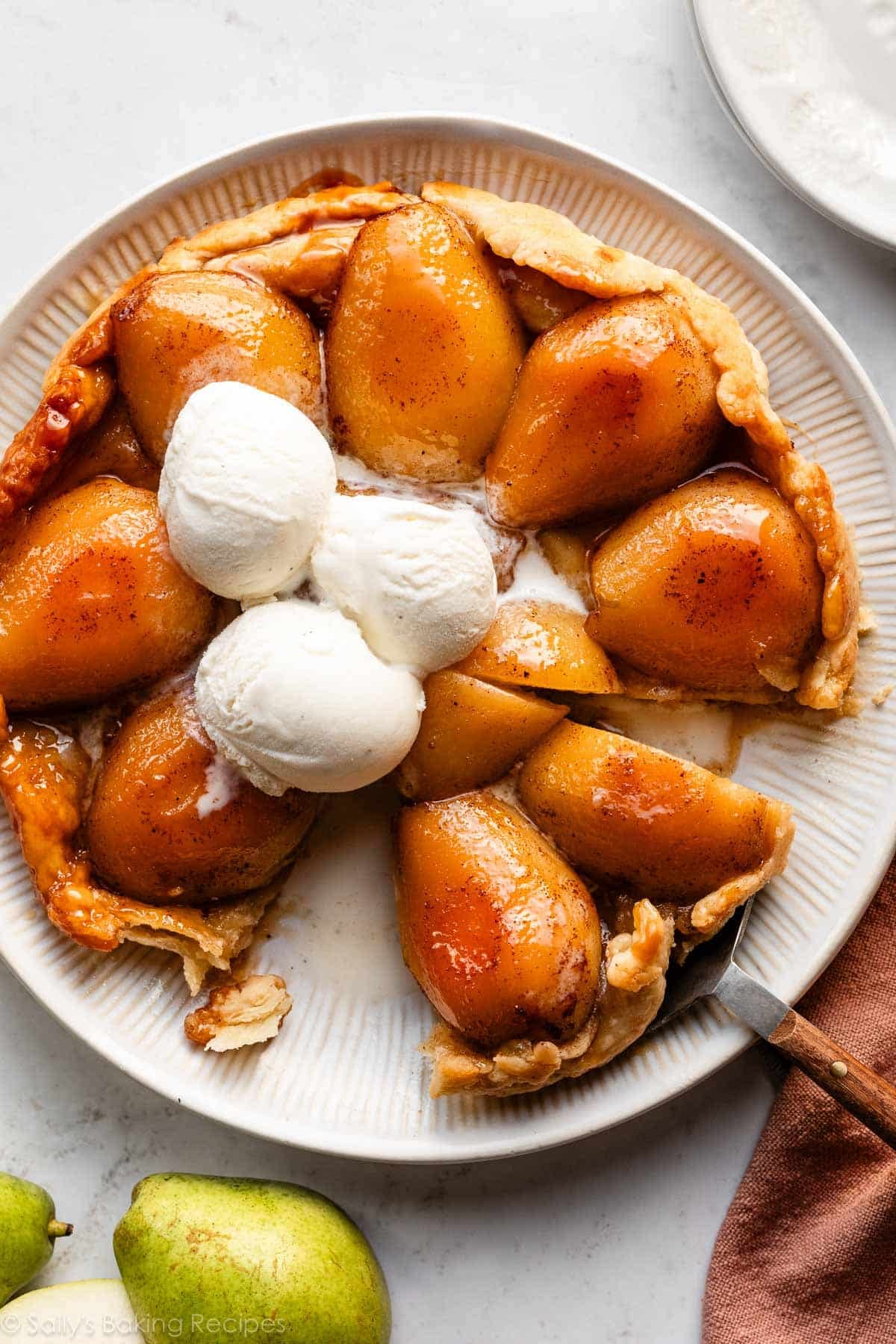 pear tarte tatin sliced on a serving plate with 3 scoops of vanilla ice cream on top.