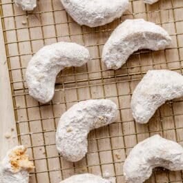 almond crescent-shaped cookies coated in powdered sugar on gold wire cooling rack.