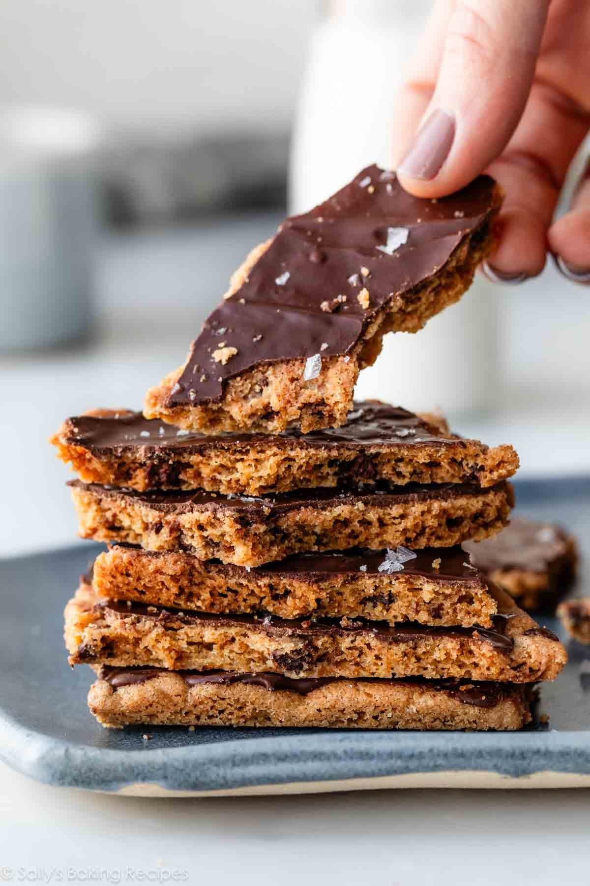 stack of chocolate chip cookie bark pieces with hand grabbing top piece.