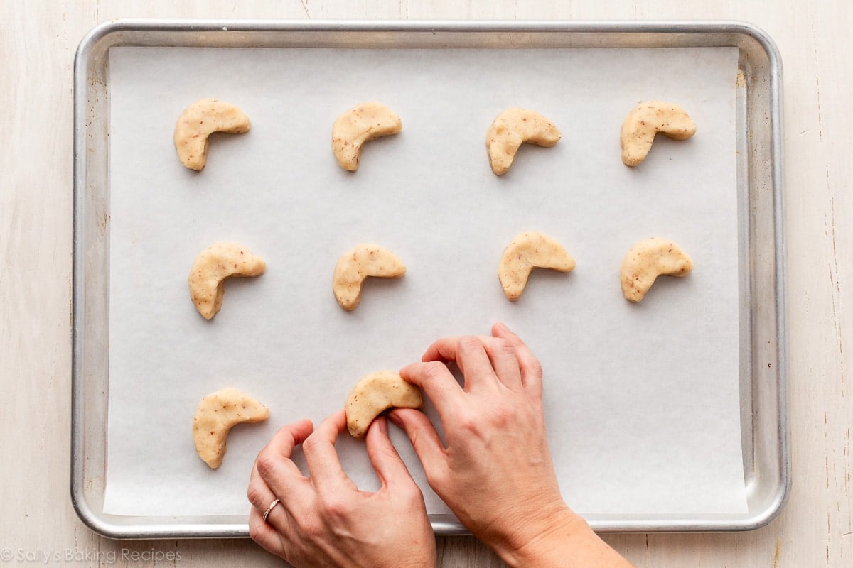 hands shaping dough into crescent moon shapes.