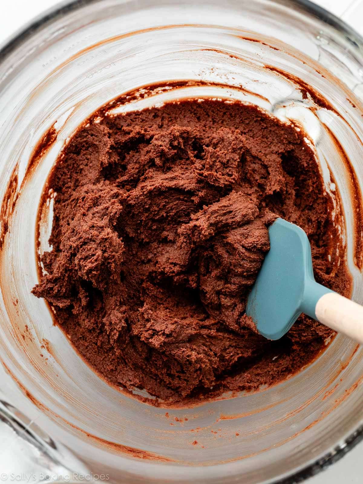 creamy chocolate cookie dough in glass bowl with blue spatula.