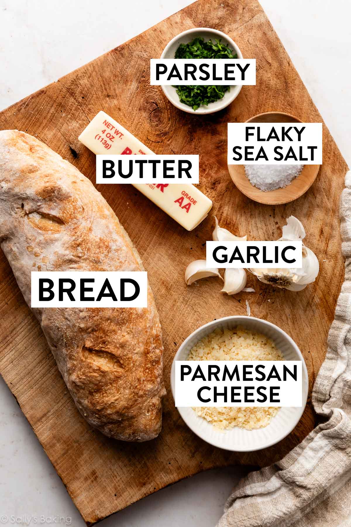 ingredients on wooden cutting board including a loaf, butter, sea salt, and parmesan cheese.