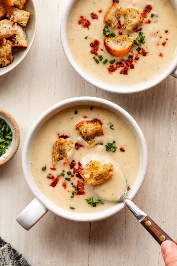 2 bowls of cauliflower potato soup with croutons, bacon, and chopped chives on top.