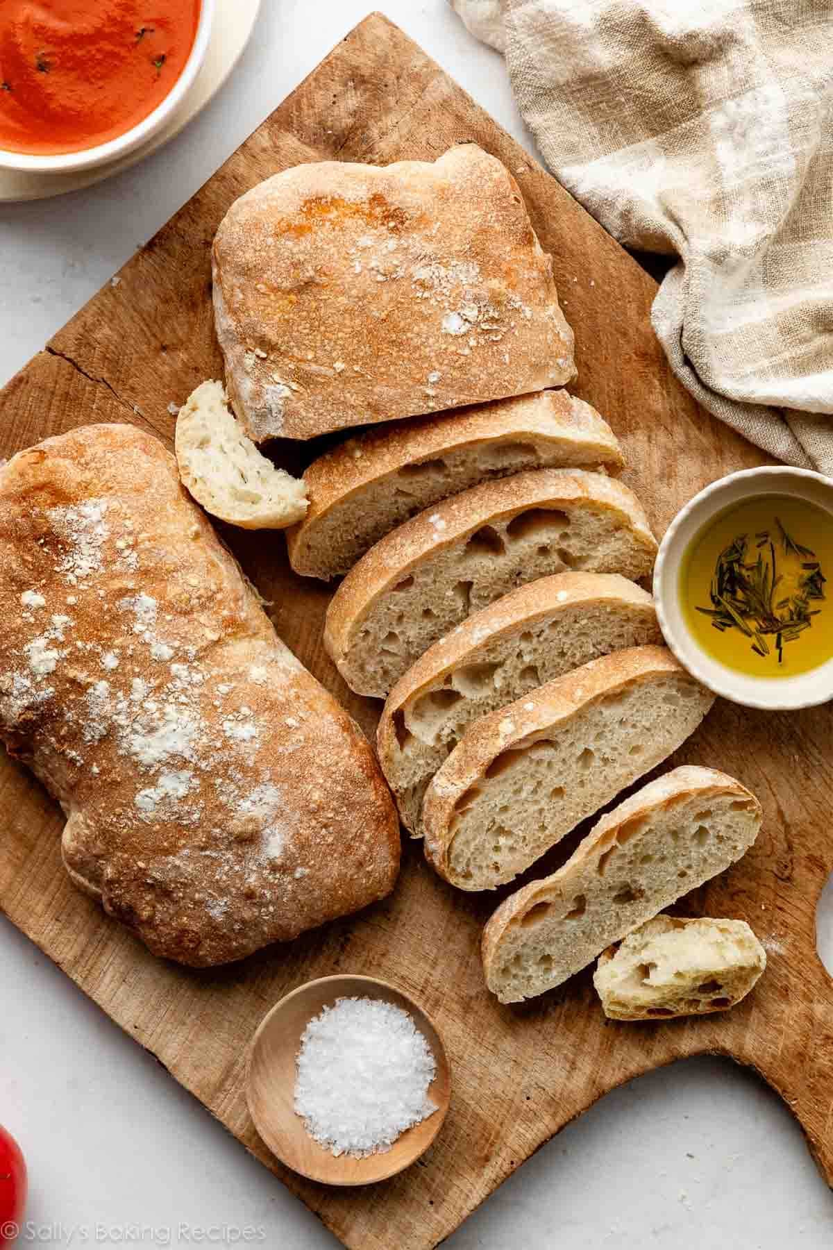ciabatta bread on wooden cutting board with sea salt and rosemary olive oil in small bowl.