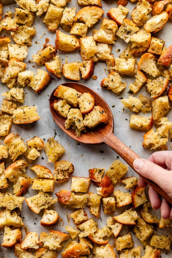 wooden spoon with homemade croutons on parchment paper lined-baking sheet.