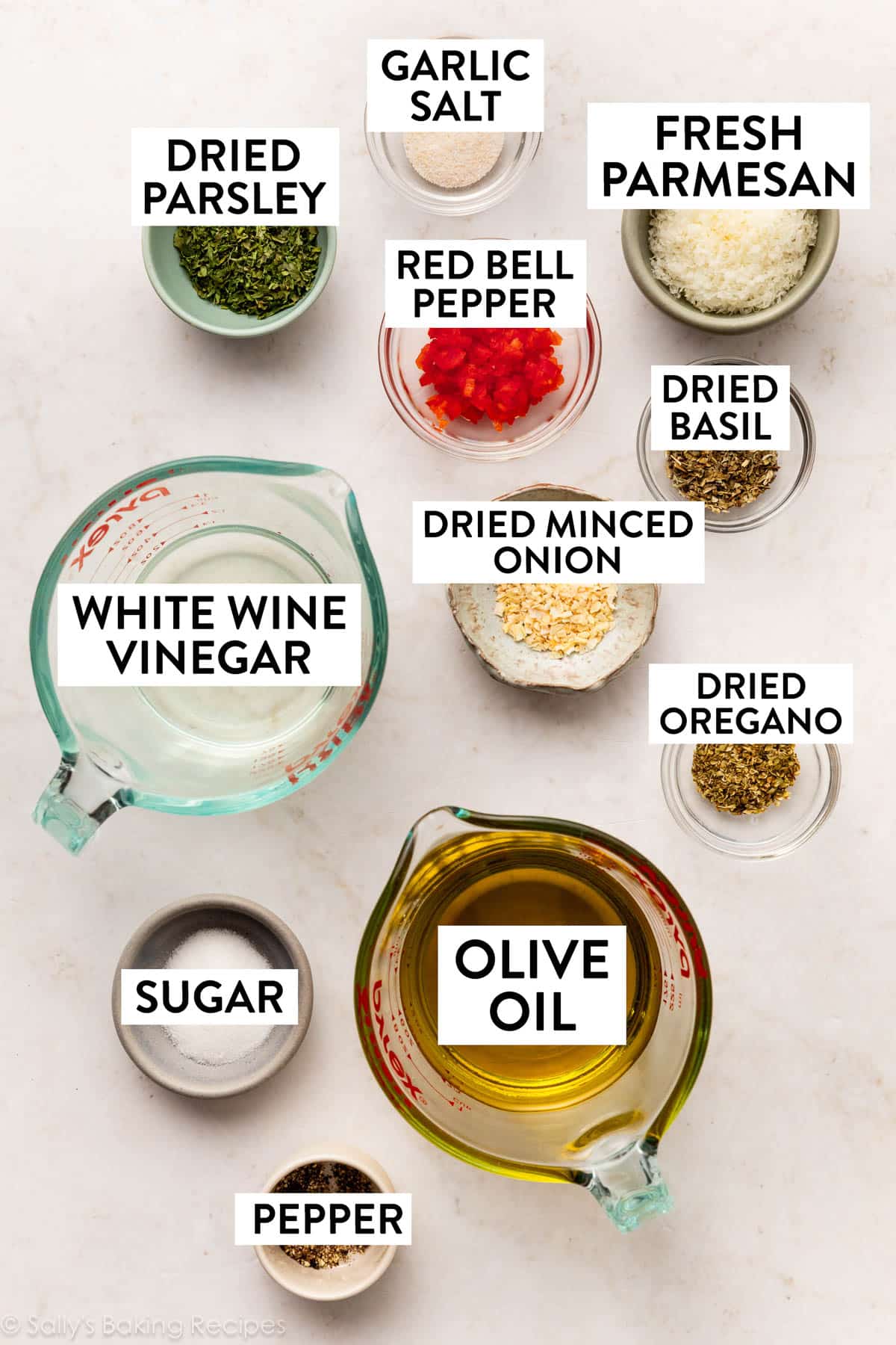 ingredients on marble surface including dried herbs, olive oil, fresh parmesan, and red bell pepper.