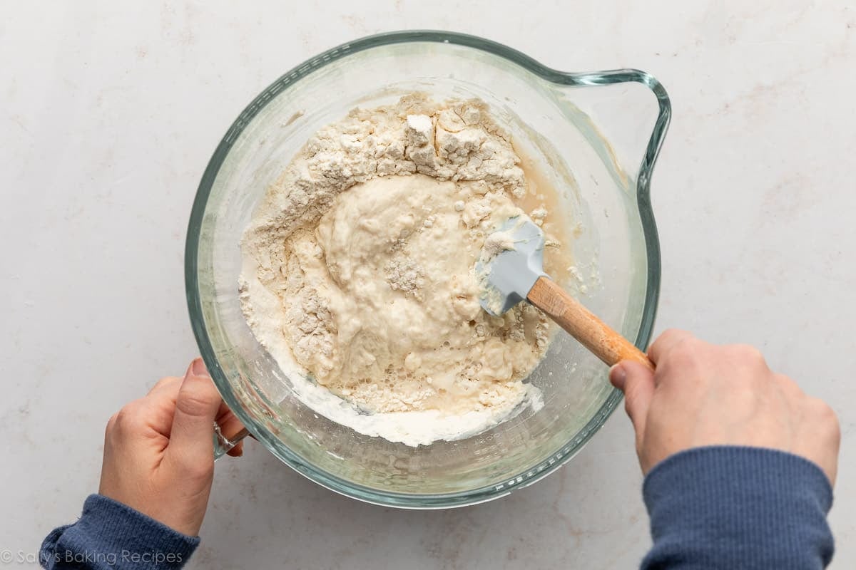 hands stirring dough ingredients in glass bowl.