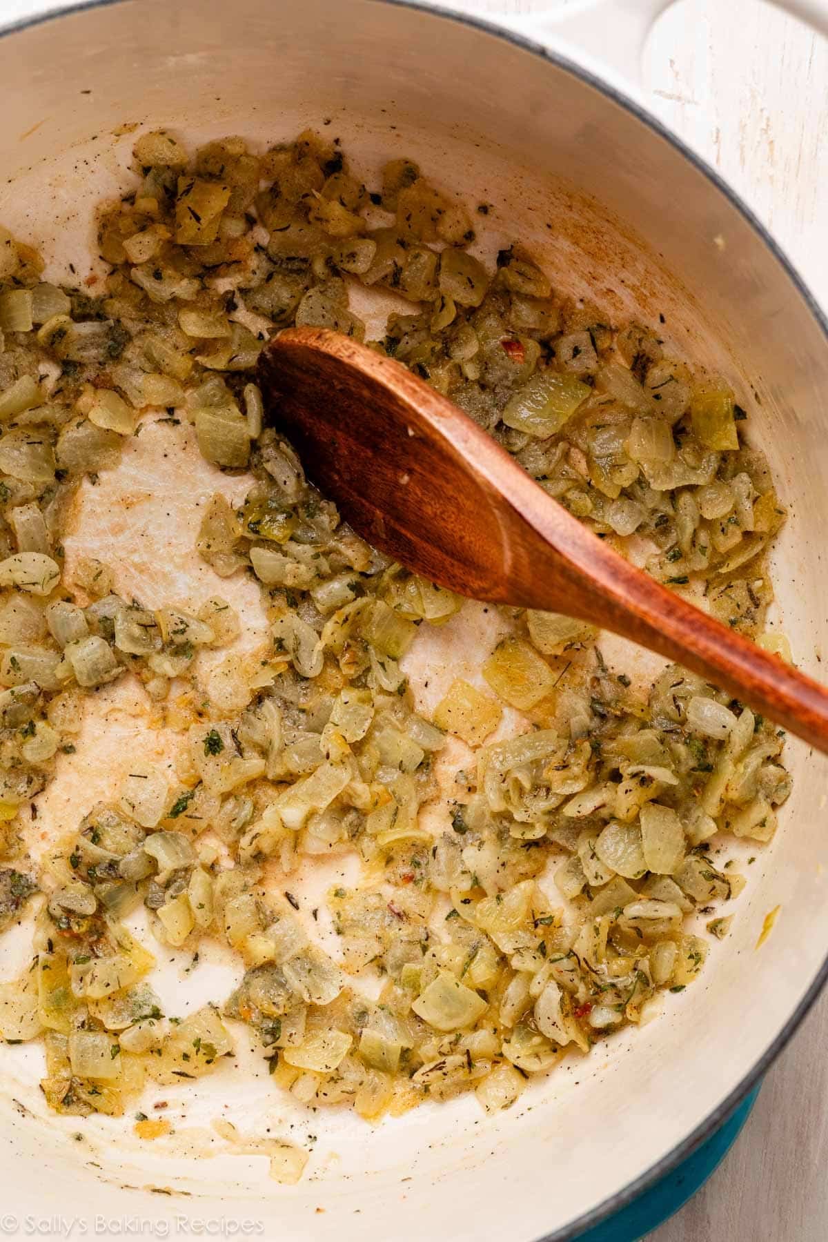 wooden spoon stirring herbed onions and garlic in pot.
