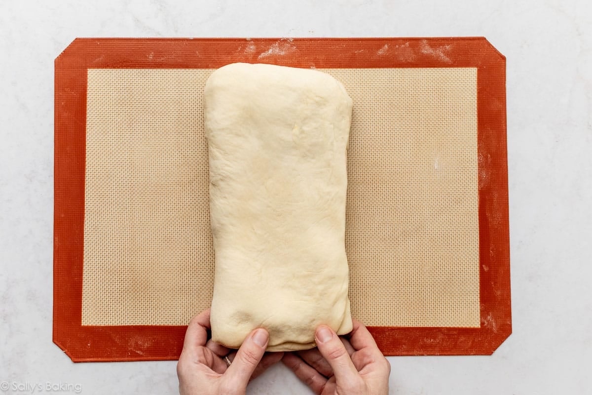 hands folding dough on top of silicone baking mat.