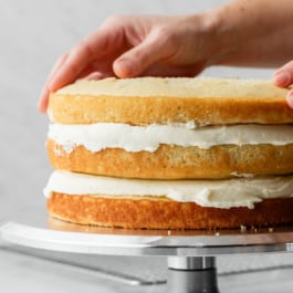 hands placing 3rd cake layer on top of a cake.