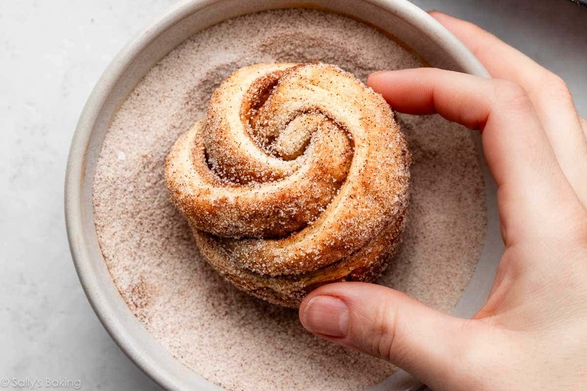 hands rolling cruffin pastry in cinnamon sugar.