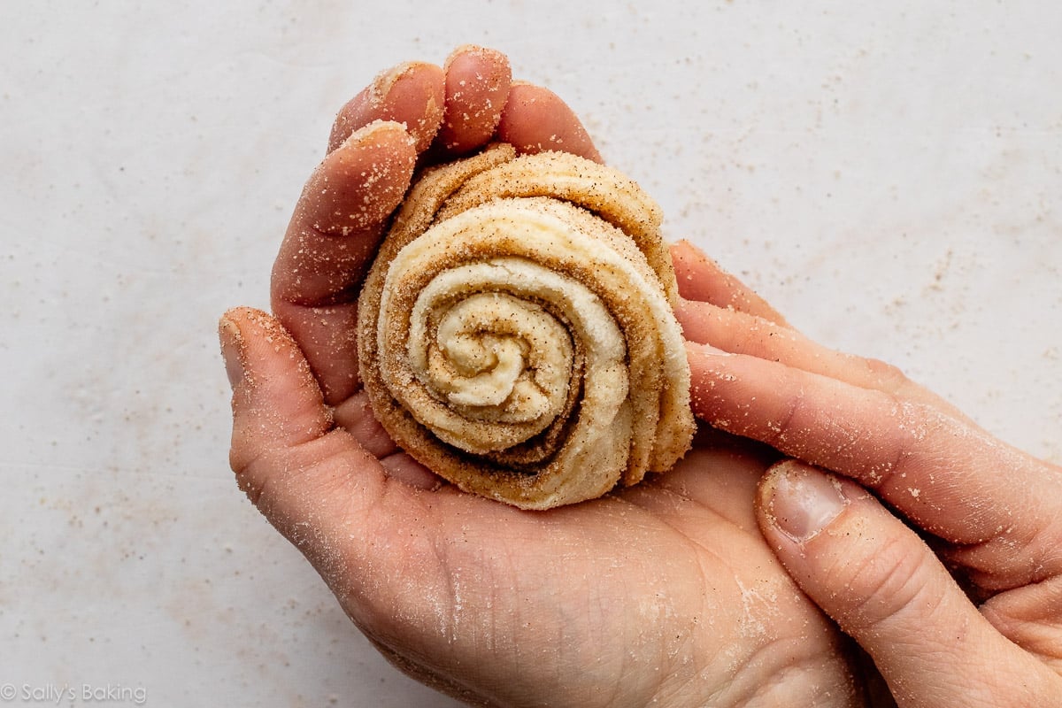 hands rolling dough in a cinnamon roll shape.