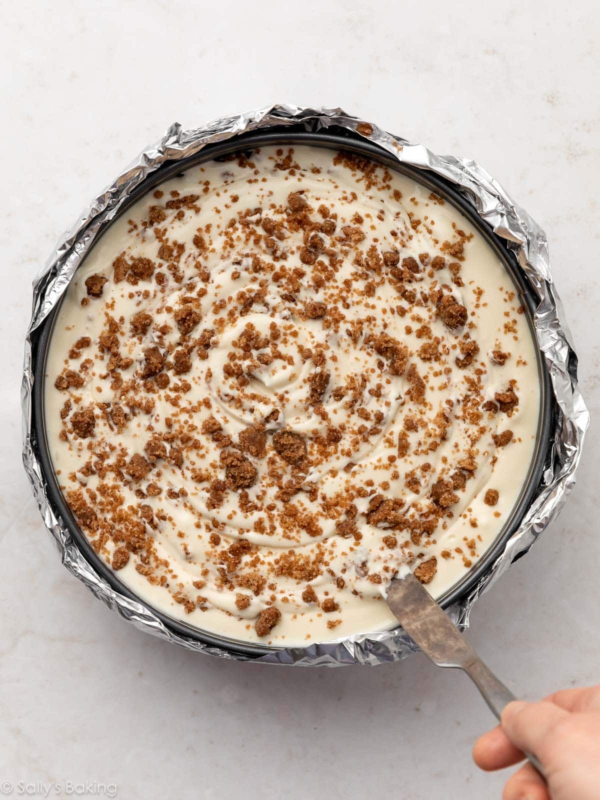 knife swirling cinnamon crumbles into cheesecake batter.