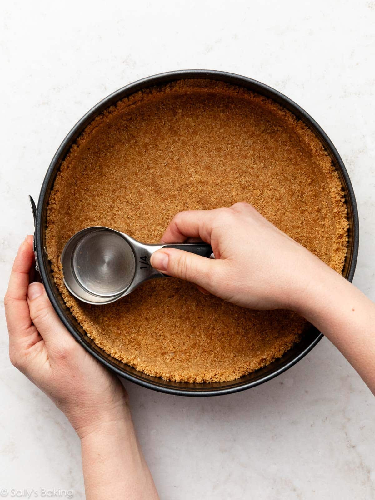 hands smoothing out graham cracker crust in springform pan.