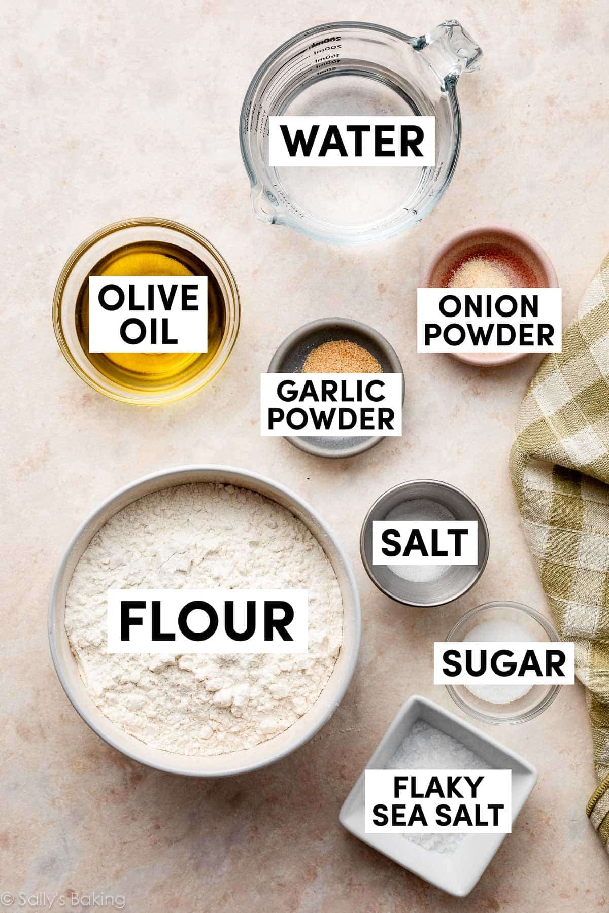 ingredients on peach-colored backdrop including flour, salt, sugar, garlic powder, water, and olive oil.