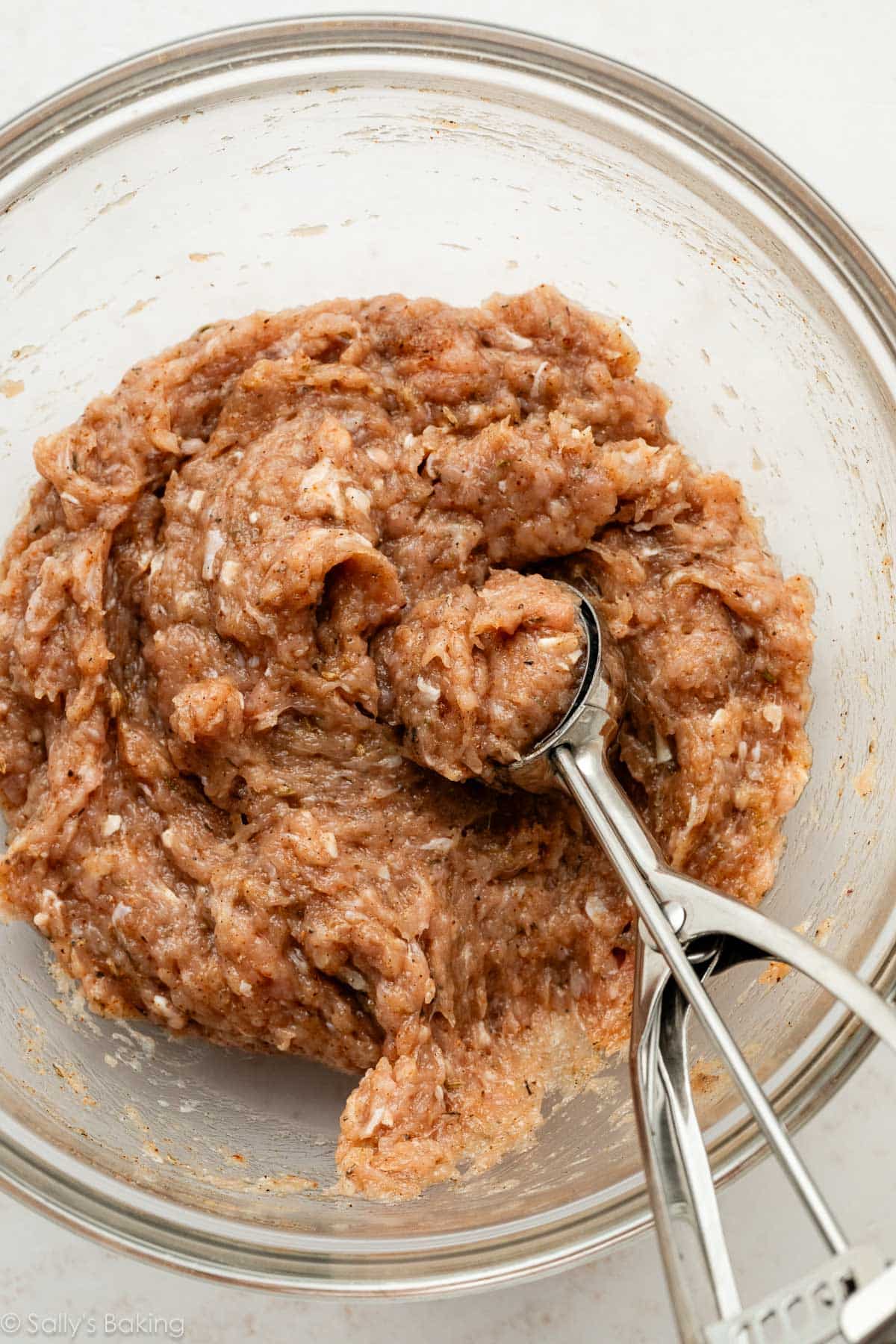 ground chicken and herb mixture with cookie scoop in glass bowl.