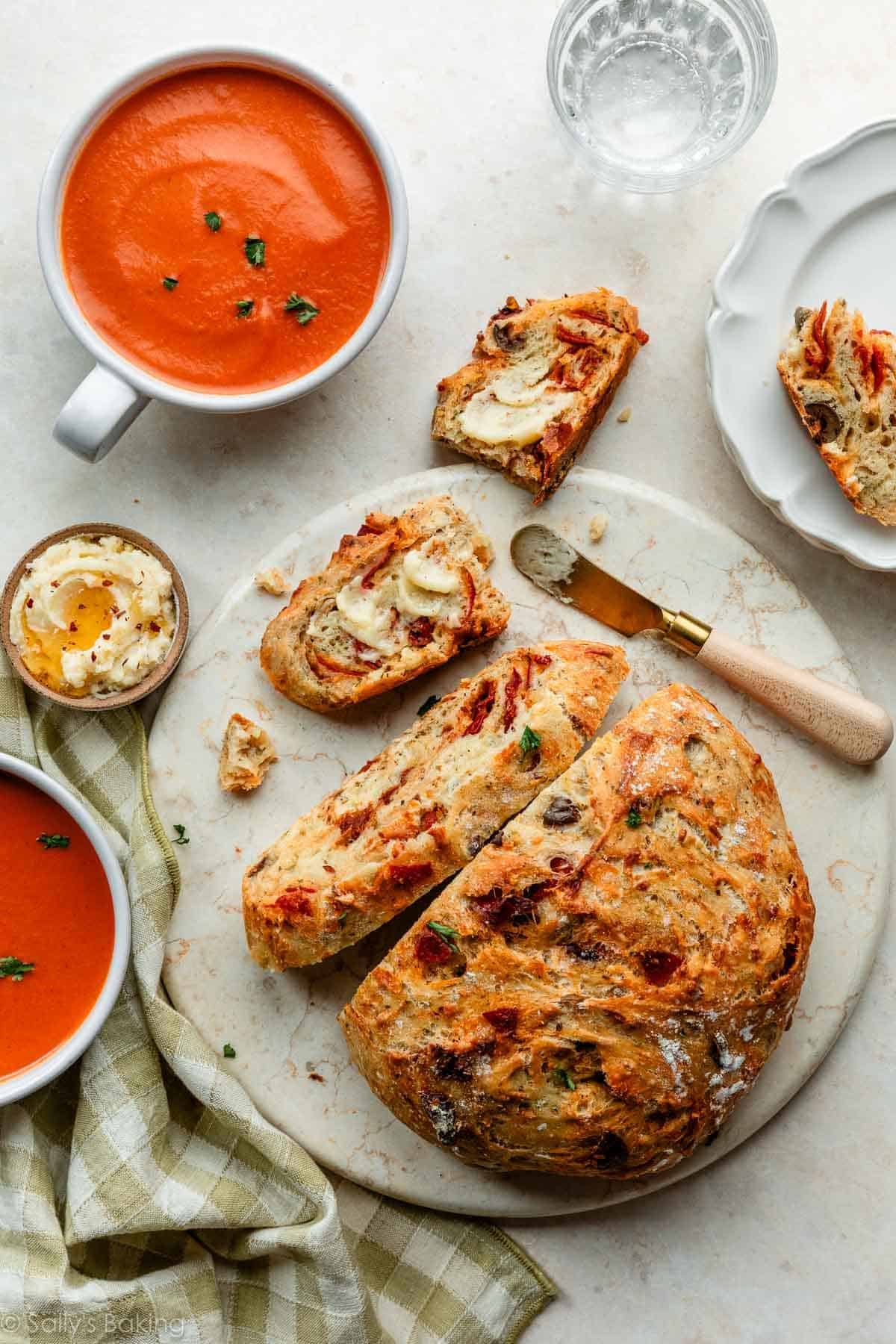 crusty bread sliced and sitting on marble circle with bowls of tomato soup.