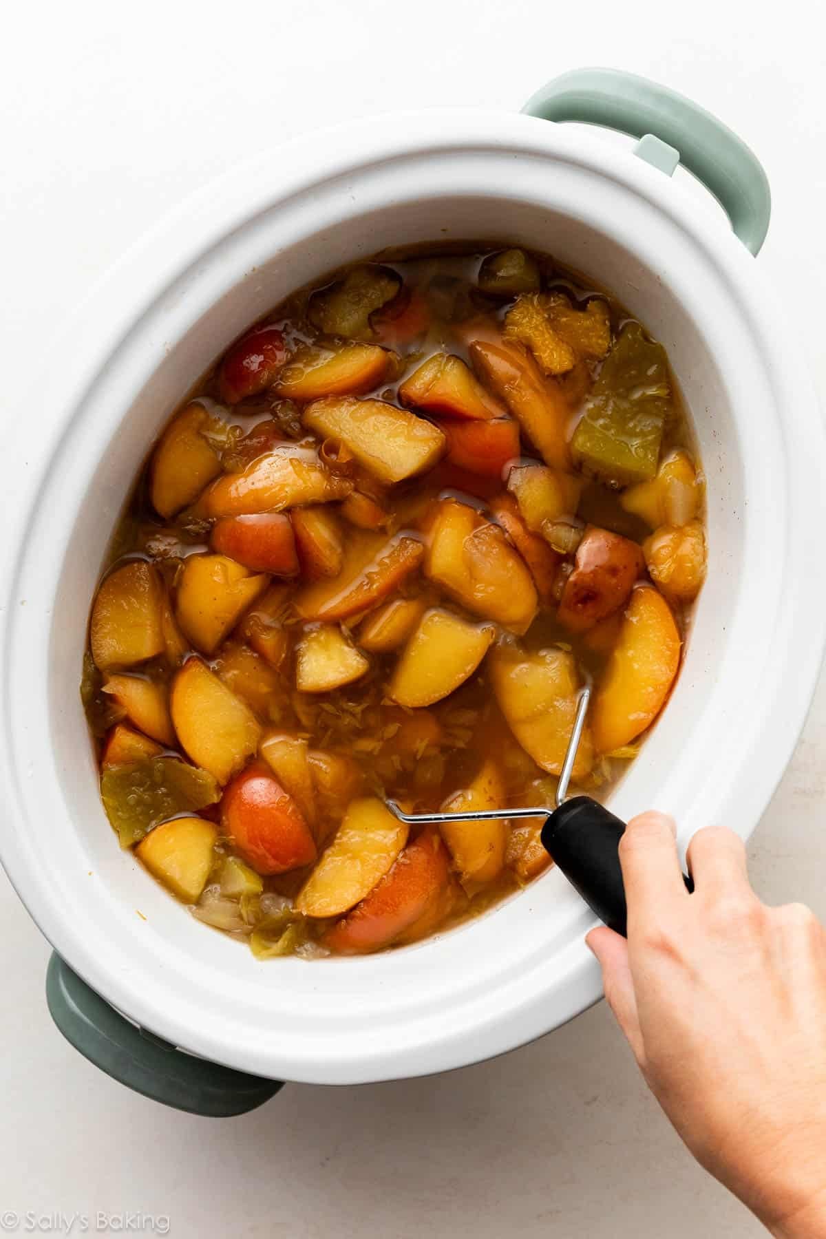 hand mashing cooked apples in slow cooker.