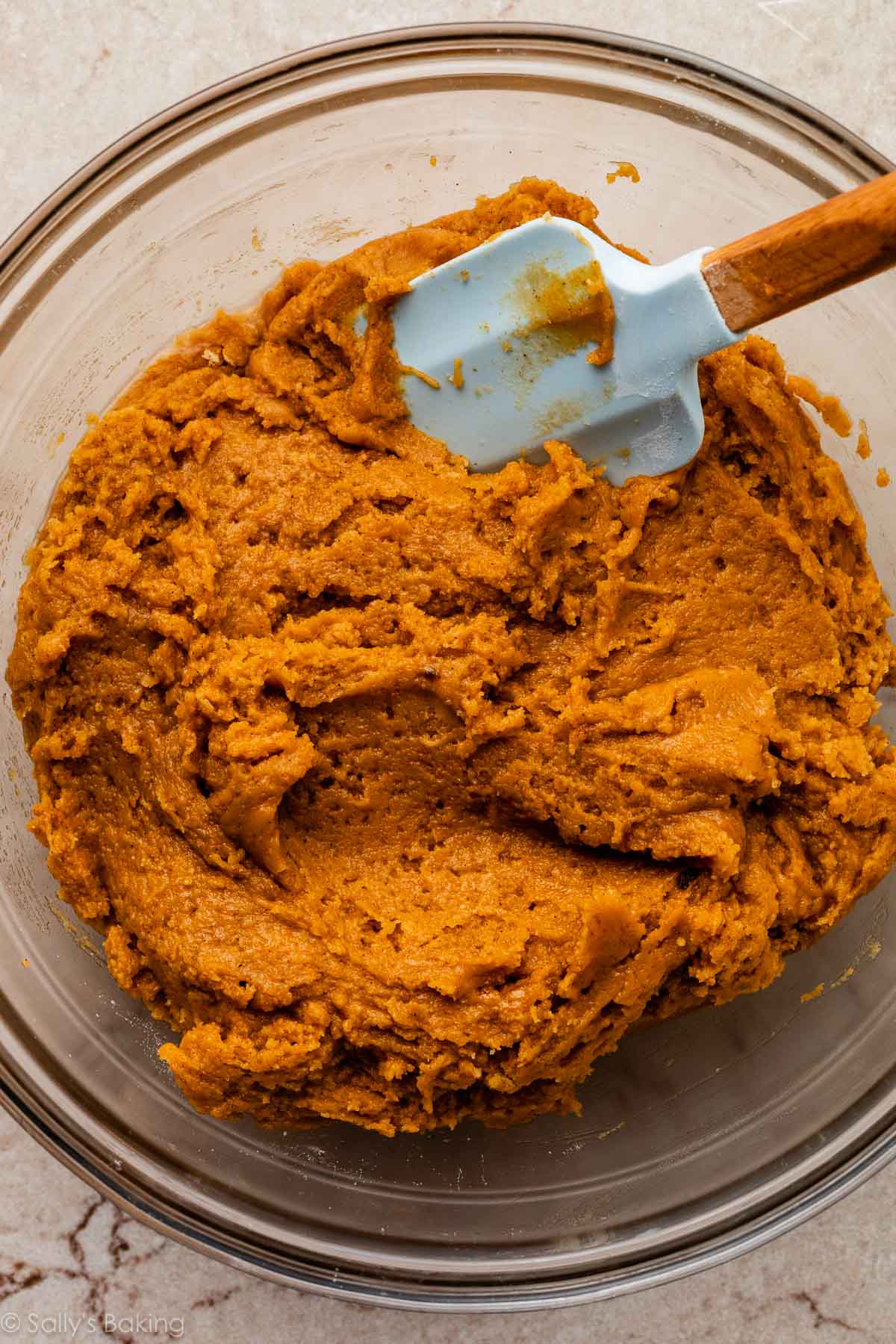 cookie dough with blue spatula in glass bowl.