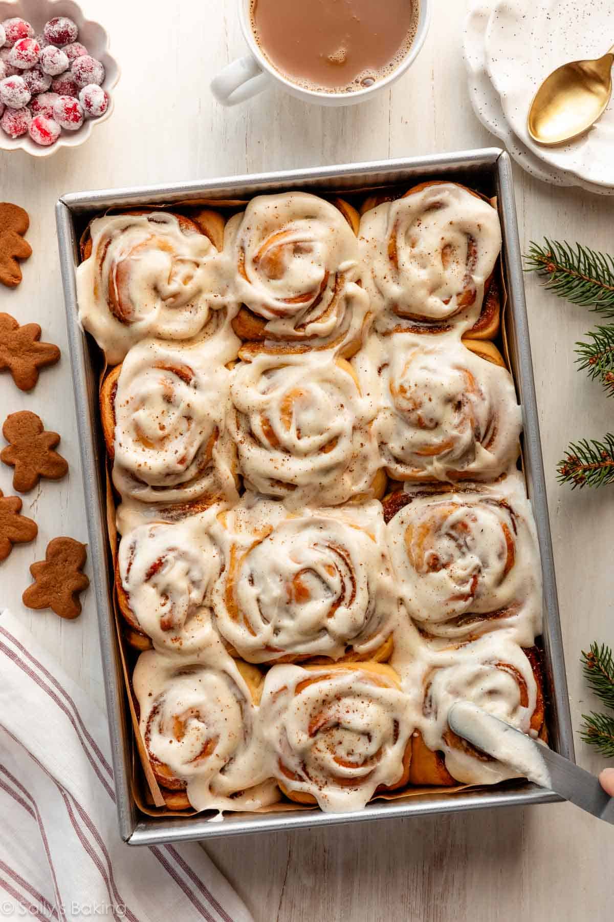 gingerbread cinnamon rolls in baking pan with sugared cranberries and mini gingerbread cookies next to it.